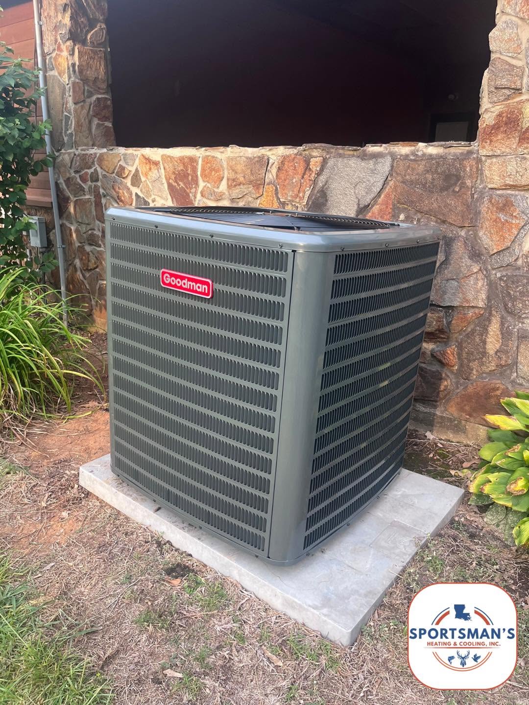 Installed outdoor HVAC condenser on a pad beside a stone wall